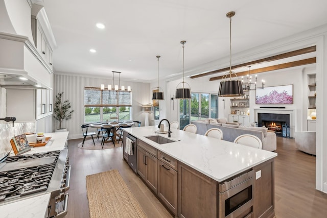 kitchen featuring an island with sink, a sink, a chandelier, wood finished floors, and appliances with stainless steel finishes