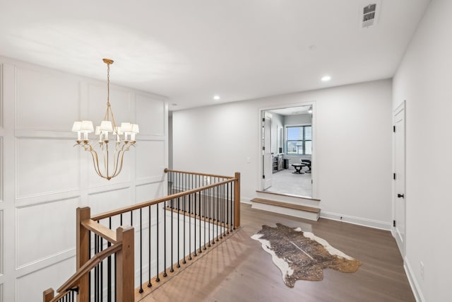 hallway with an upstairs landing, recessed lighting, an inviting chandelier, baseboards, and wood finished floors