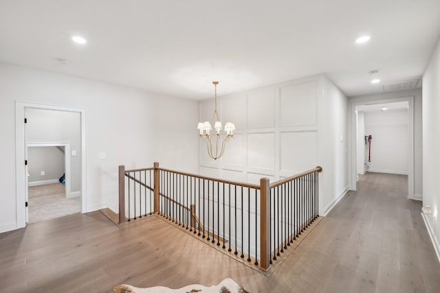 corridor with a chandelier, a decorative wall, an upstairs landing, and light wood-style flooring