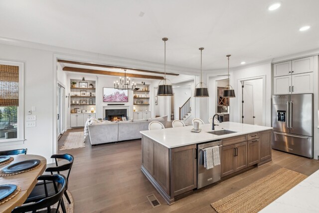 kitchen featuring light countertops, a sink, a warm lit fireplace, appliances with stainless steel finishes, and wood finished floors