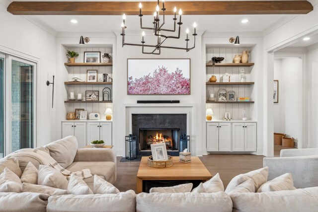 living area featuring dark wood-style flooring, a chandelier, beamed ceiling, built in features, and a lit fireplace
