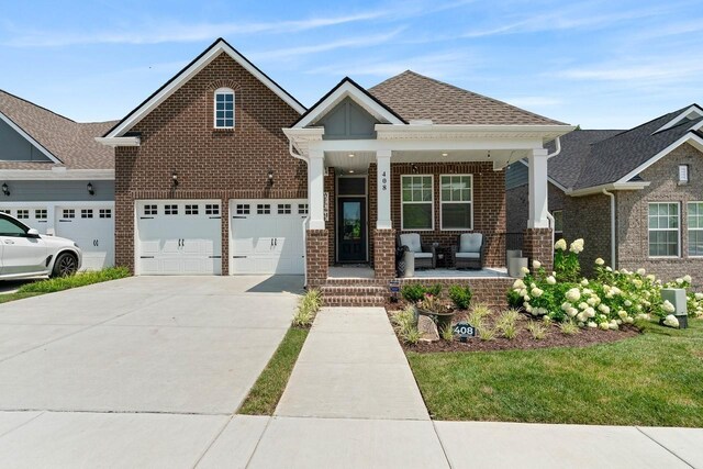 craftsman-style home with driveway, brick siding, a shingled roof, and a porch