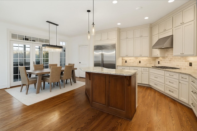 kitchen featuring tasteful backsplash, stainless steel built in fridge, wall chimney range hood, a kitchen island, and dark wood-type flooring
