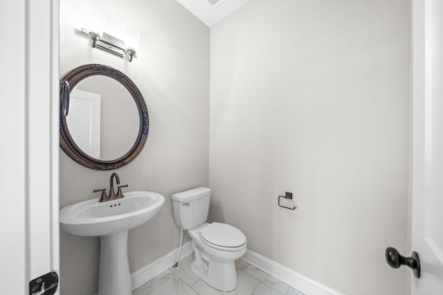 half bathroom with marble finish floor, toilet, and baseboards