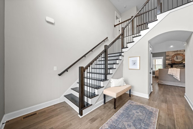 staircase with arched walkways, a high ceiling, wood finished floors, and baseboards