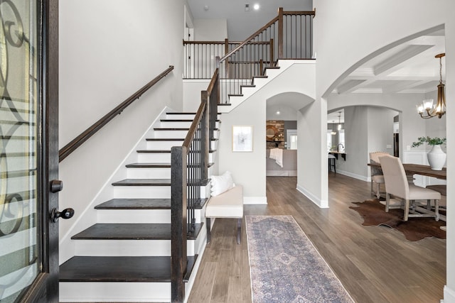 entryway with coffered ceiling, stairway, wood finished floors, baseboards, and arched walkways