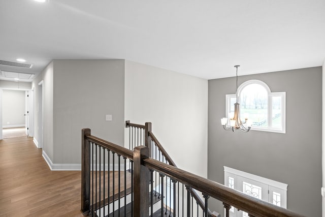 hallway with an upstairs landing, attic access, wood finished floors, baseboards, and visible vents