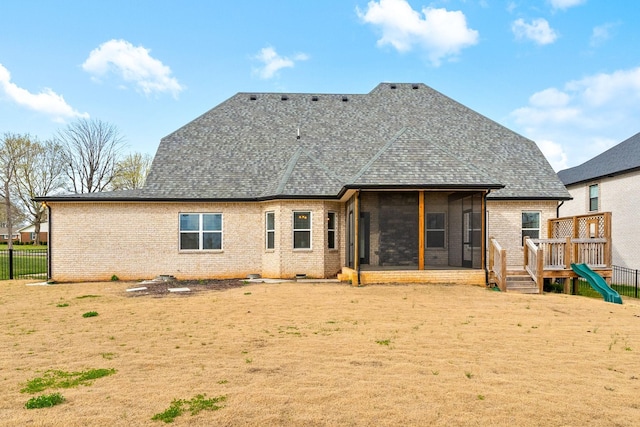 back of house featuring brick siding, a sunroom, fence, and roof with shingles