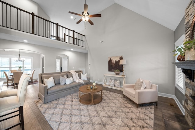 living area with arched walkways, wood finished floors, ceiling fan with notable chandelier, and a stone fireplace