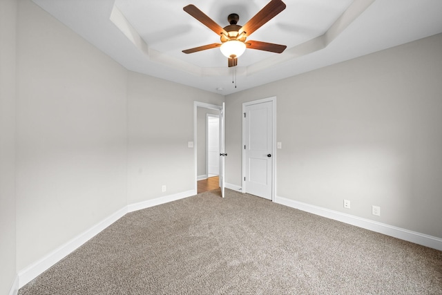 carpeted spare room with baseboards, a tray ceiling, and ceiling fan