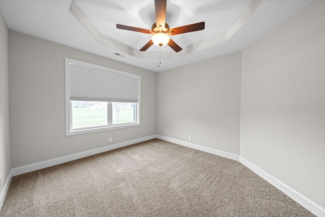carpeted spare room featuring baseboards, ceiling fan, visible vents, and a raised ceiling