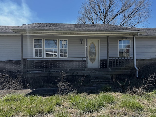 view of front of home with covered porch, brick siding, and roof with shingles
