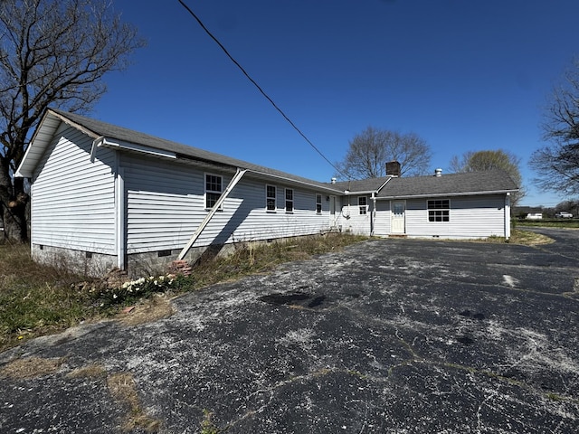 rear view of property with crawl space, aphalt driveway, and a chimney