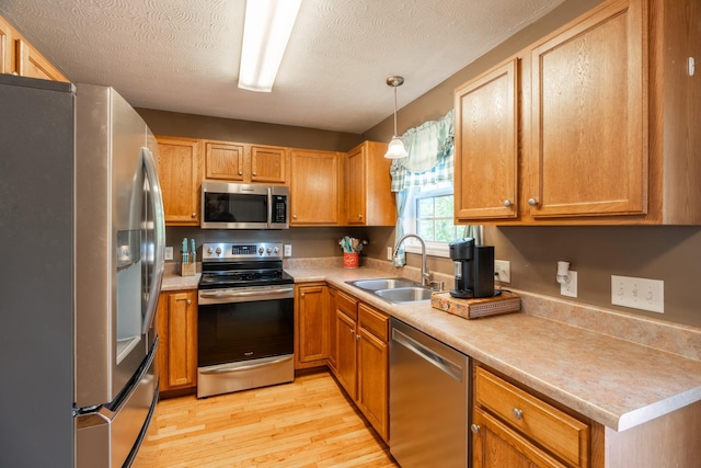 kitchen featuring a textured ceiling, light countertops, appliances with stainless steel finishes, a sink, and light wood-type flooring