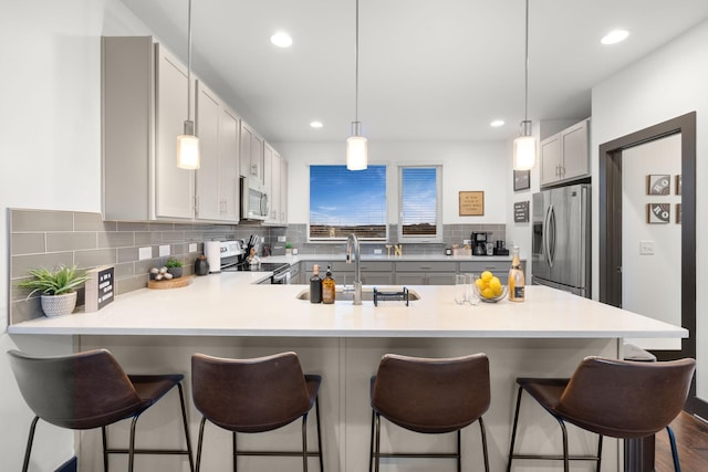 kitchen with light countertops, tasteful backsplash, a sink, a peninsula, and appliances with stainless steel finishes