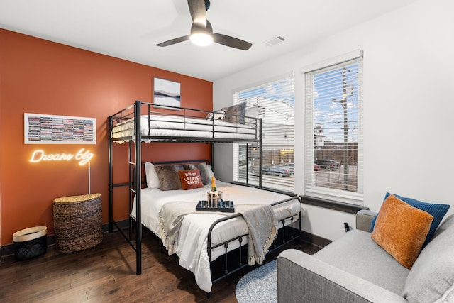 bedroom with a ceiling fan, visible vents, baseboards, and wood finished floors