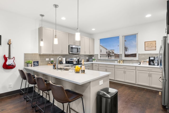 kitchen with a kitchen breakfast bar, tasteful backsplash, dark wood-style flooring, a peninsula, and appliances with stainless steel finishes