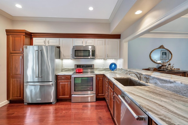 kitchen featuring light stone countertops, ornamental molding, stainless steel appliances, dark wood finished floors, and a sink