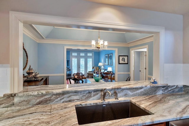 kitchen featuring crown molding, light stone countertops, a sink, french doors, and a notable chandelier