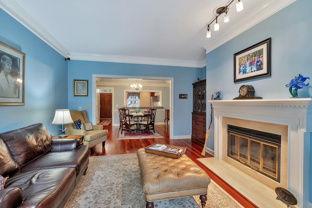 living room featuring crown molding, wood finished floors, a glass covered fireplace, baseboards, and an inviting chandelier