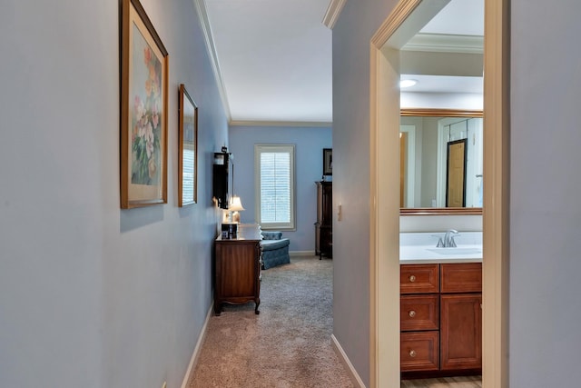 hallway with baseboards, a sink, crown molding, and light colored carpet