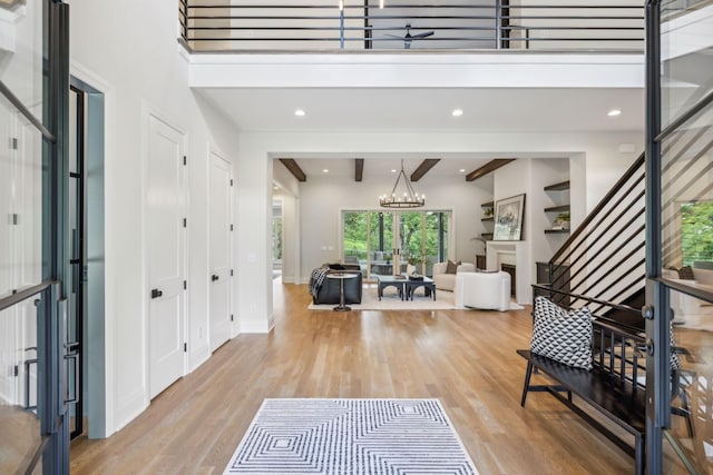 foyer featuring a chandelier, a towering ceiling, beamed ceiling, and light wood finished floors