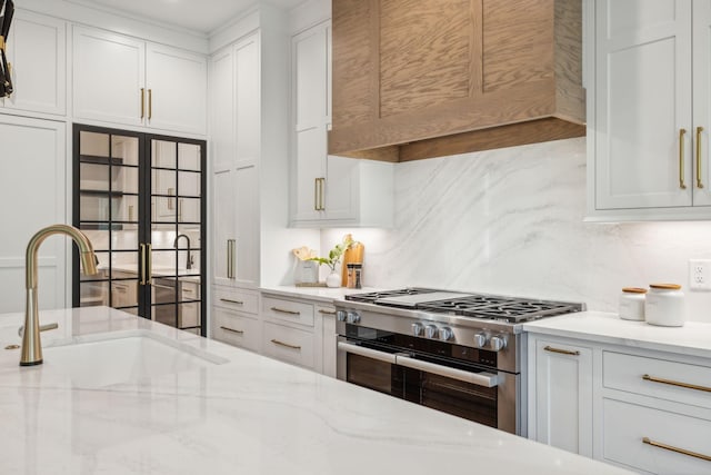 kitchen with decorative backsplash, white cabinetry, a sink, custom range hood, and double oven range
