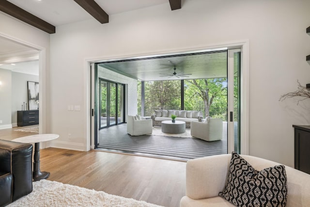 living area with baseboards, wood finished floors, beam ceiling, and a ceiling fan