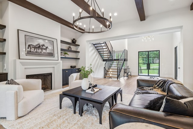 living room with stairway, light wood-type flooring, a chandelier, beamed ceiling, and a fireplace