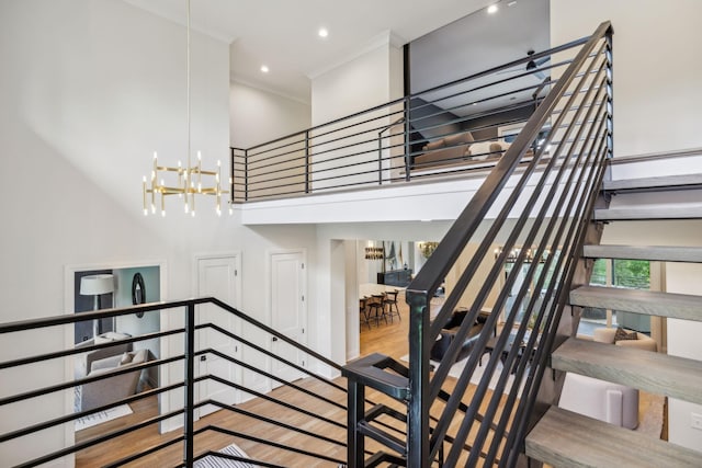 staircase featuring crown molding, wood finished floors, a towering ceiling, recessed lighting, and an inviting chandelier