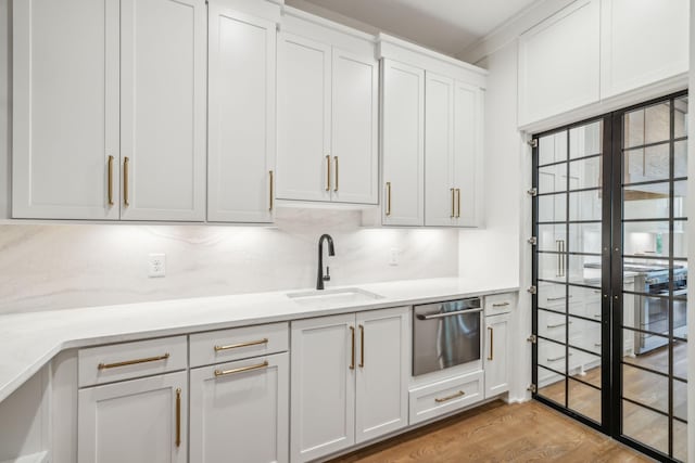kitchen featuring a warming drawer, backsplash, a sink, white cabinets, and wood finished floors