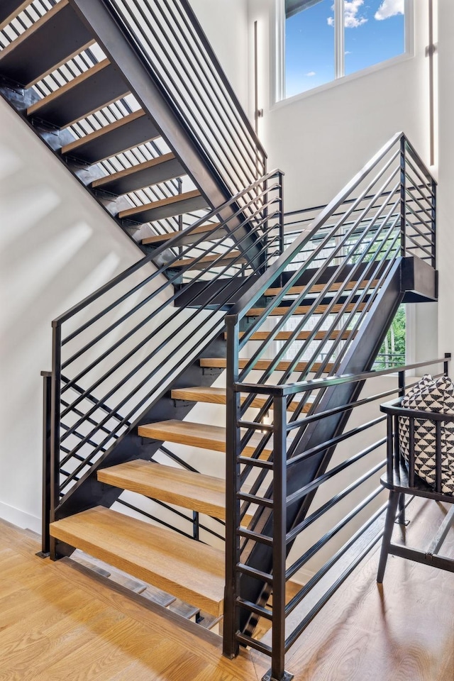 stairs featuring wood finished floors, a towering ceiling, and a healthy amount of sunlight