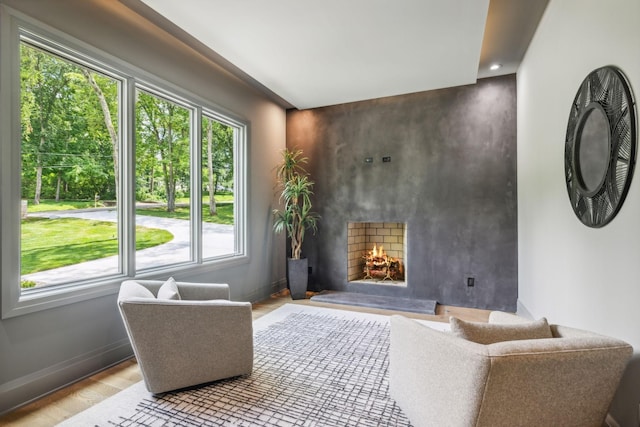 living area with baseboards, a warm lit fireplace, wood finished floors, and an accent wall