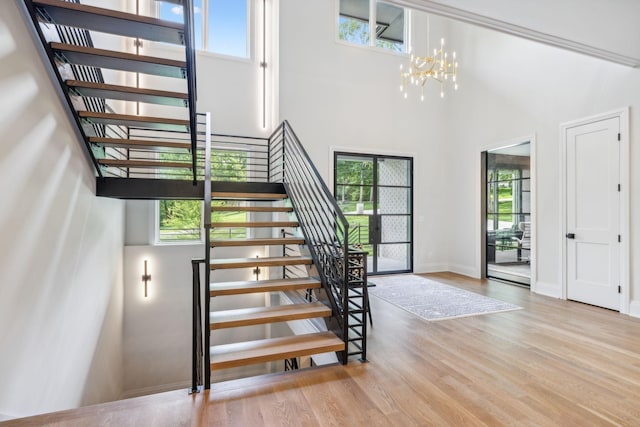 stairs with baseboards, wood finished floors, a towering ceiling, and a chandelier