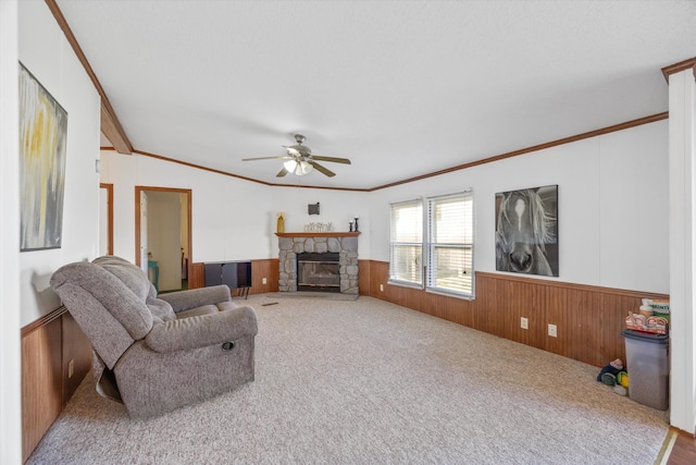 carpeted living area featuring wood walls, ornamental molding, a ceiling fan, a fireplace, and wainscoting
