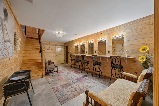 bar with concrete flooring, wood walls, stairway, and bar