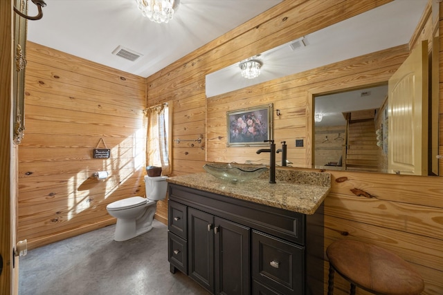 bathroom featuring visible vents, wooden walls, toilet, vanity, and concrete flooring