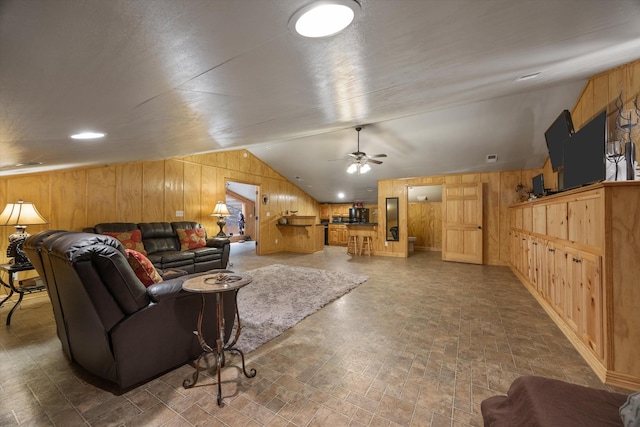 living room with a ceiling fan, wooden walls, and vaulted ceiling