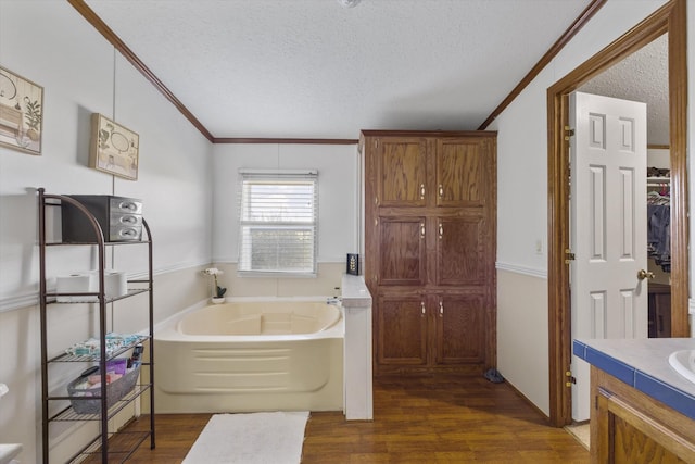 bathroom with a textured ceiling, ornamental molding, wood finished floors, vanity, and a garden tub