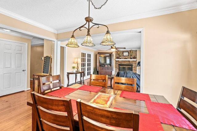 dining area with a textured ceiling, a brick fireplace, ornamental molding, a ceiling fan, and light wood-style floors