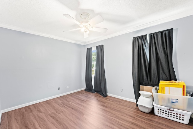 unfurnished room featuring a ceiling fan, wood finished floors, a textured ceiling, baseboards, and ornamental molding