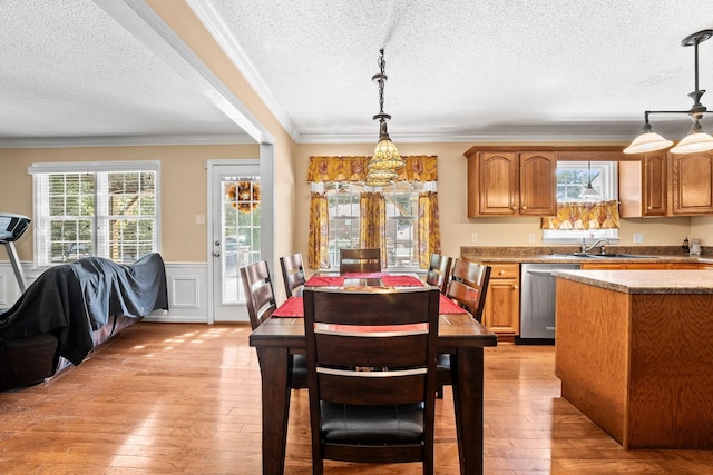 dining area with wainscoting, crown molding, a textured ceiling, and light wood-type flooring