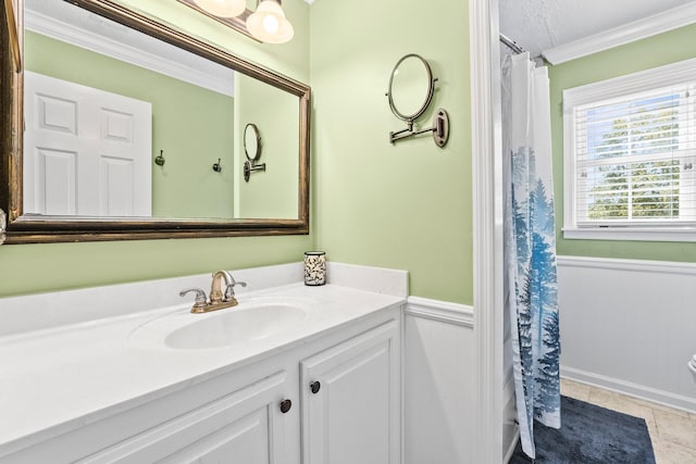 bathroom with a wainscoted wall, a textured ceiling, ornamental molding, tile patterned floors, and vanity