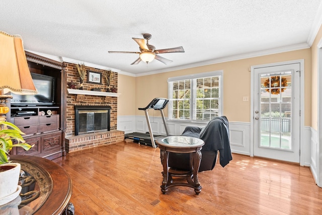exercise room featuring wood finished floors, ornamental molding, a fireplace, and ceiling fan
