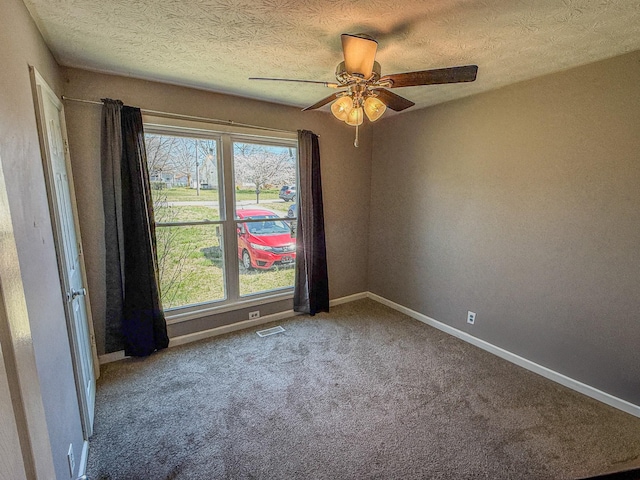 carpeted empty room with baseboards, a textured ceiling, ceiling fan, and visible vents