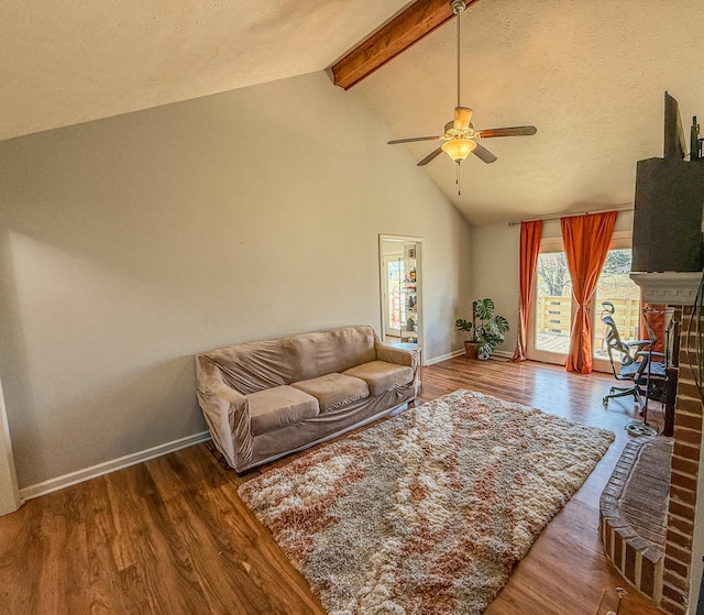 living room featuring a ceiling fan, a fireplace, wood finished floors, baseboards, and beamed ceiling