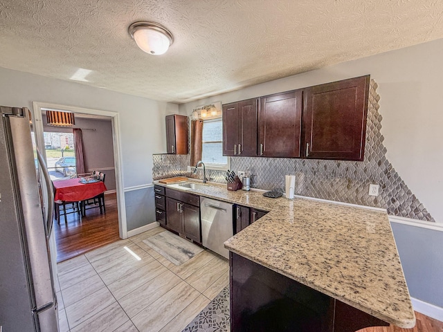 kitchen featuring stainless steel appliances, backsplash, a sink, light stone counters, and dark brown cabinets