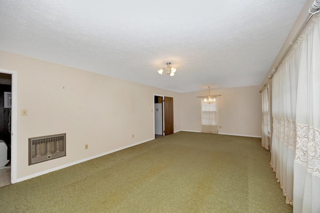 empty room featuring light colored carpet, an inviting chandelier, baseboards, a textured ceiling, and heating unit