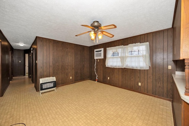 unfurnished room with heating unit, a ceiling fan, wooden walls, a textured ceiling, and baseboards