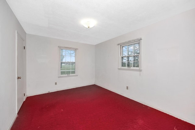 spare room with a wealth of natural light, dark colored carpet, baseboards, and a textured ceiling